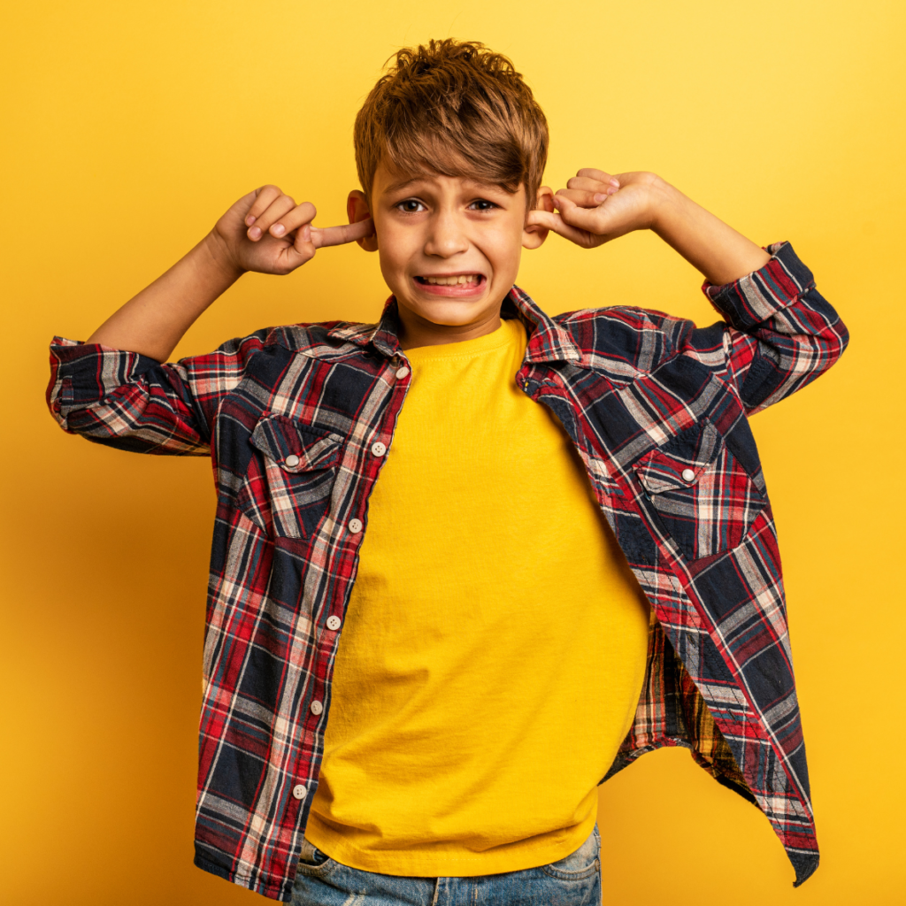 kind van 10 jaar met geel shirt en geruite blouse eroverheen, met vingers in de horen en gezichtsuitdrukking van schrikken
